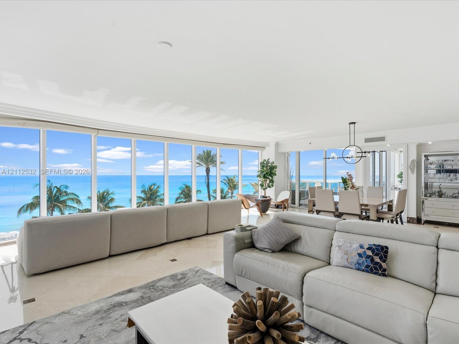 Open-concept living space featuring floor-to-ceiling glass windows, polished stone flooring, and expansive ocean and coastal scenery Open-concept living space featuring floor-to-ceiling glass windows, polished stone flooring, and expansive ocean and coastal scenery