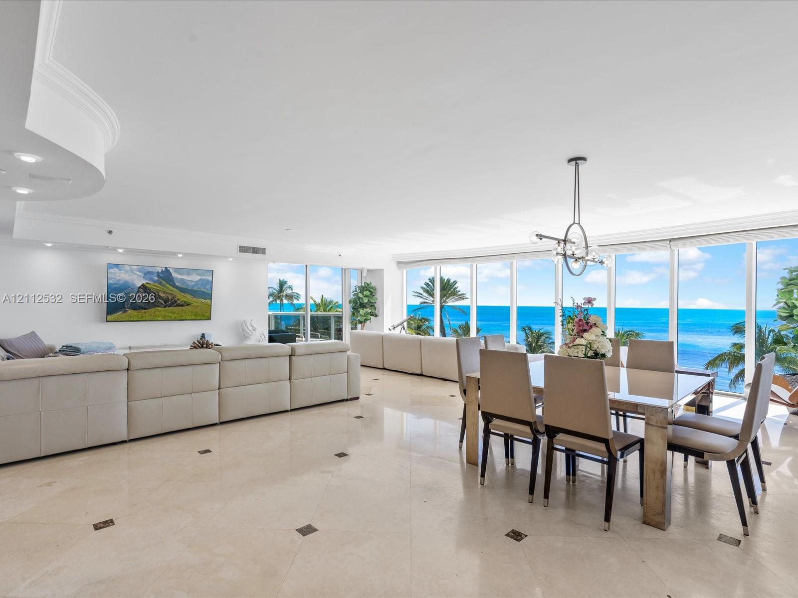 Open-concept floor plan featuring expansive floor-to-ceiling windows, polished stone tile flooring with decorative inlay, recessed lighting, and a modern tiered ceiling detail Open-concept floor plan featuring expansive floor-to-ceiling windows, polished stone tile flooring with decorative inlay, recessed lighting, and a modern tiered ceiling detail