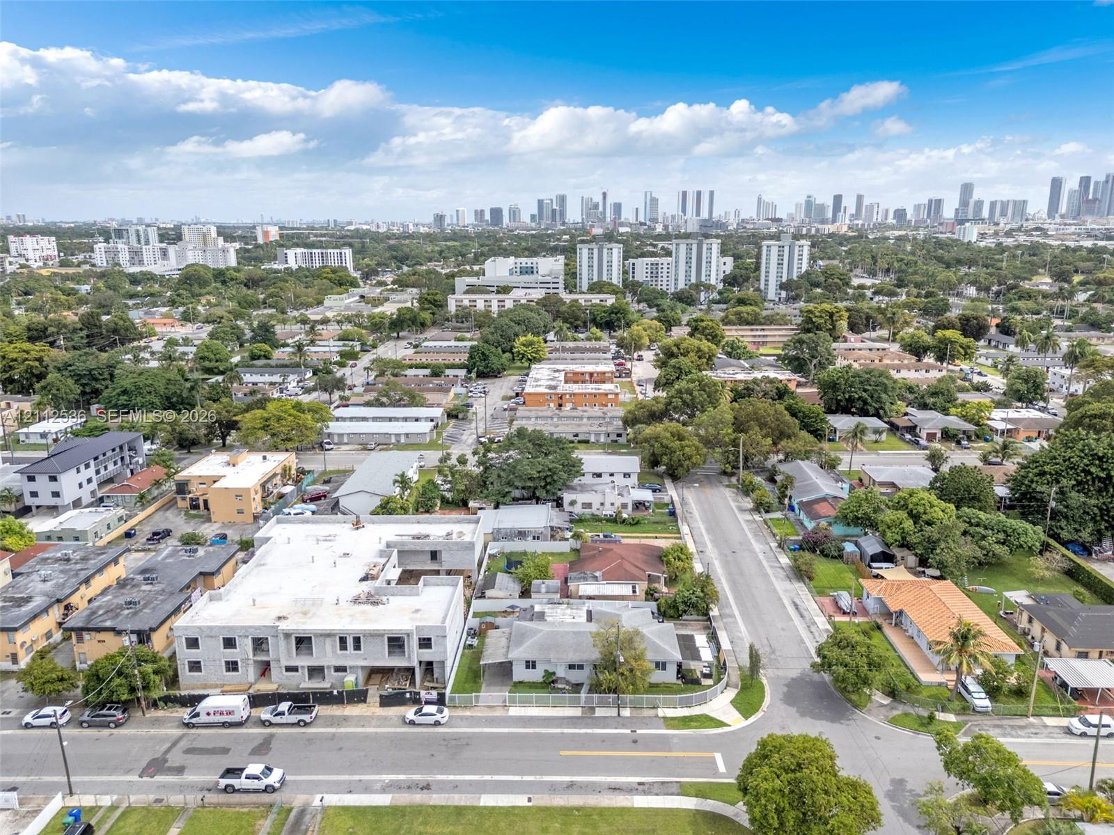 Aerial perspective of urban neighborhood featuring high-rise city skyline, paved street infrastructure, and established greenery
