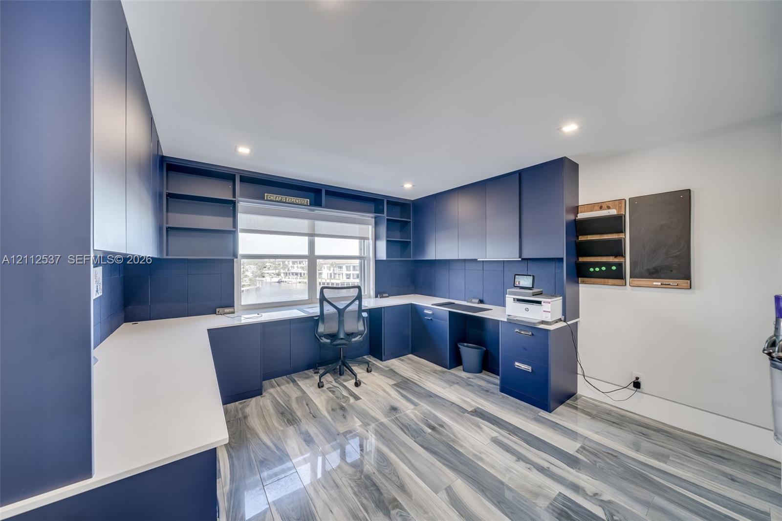 Custom built-in navy cabinetry with integrated shelving, white solid surface countertops, recessed ceiling lighting, and wood-finish flooring