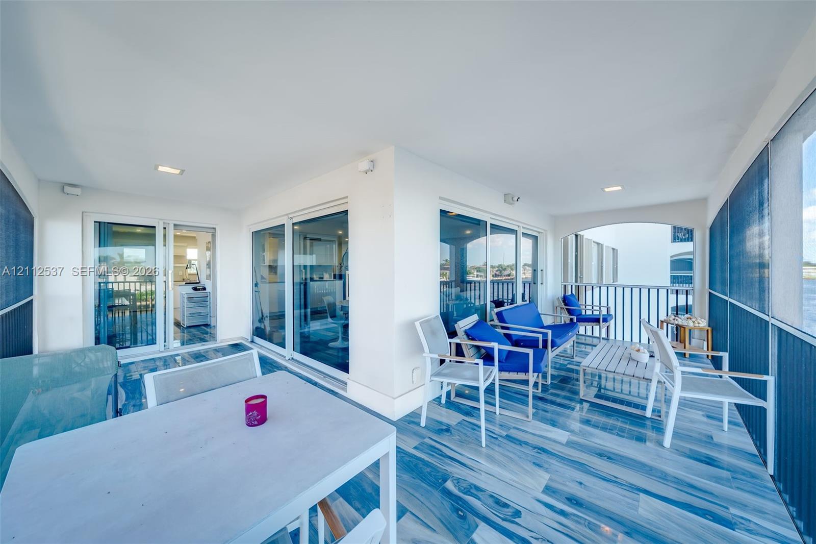 Covered balcony featuring multi-panel glass sliding doors, tiled flooring, recessed lighting, and metal railing