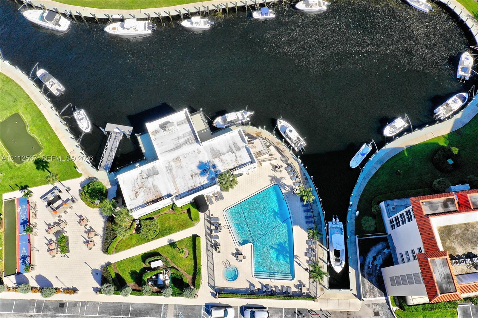 Aerial perspective of a waterfront property featuring a swimming pool, integrated spa, private boat slips, and paved terrace area