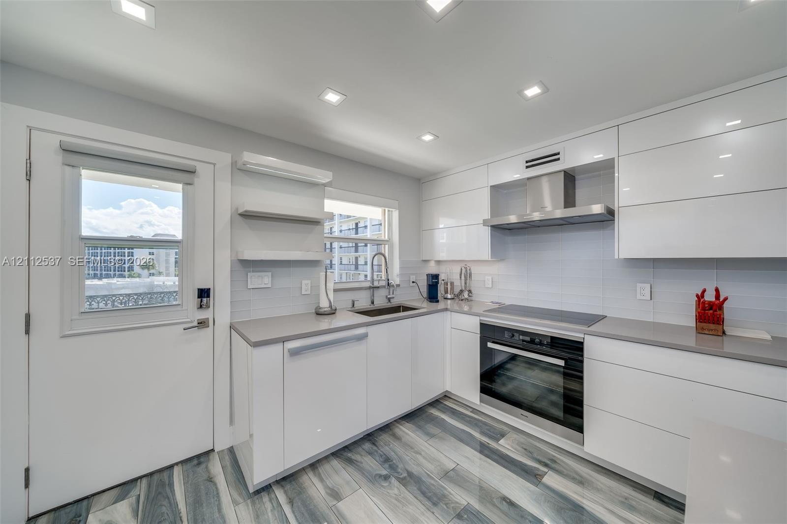 Kitchen featuring high-gloss white cabinetry, quartz countertops, stainless steel appliances, recessed lighting, and wood-finish tile flooring