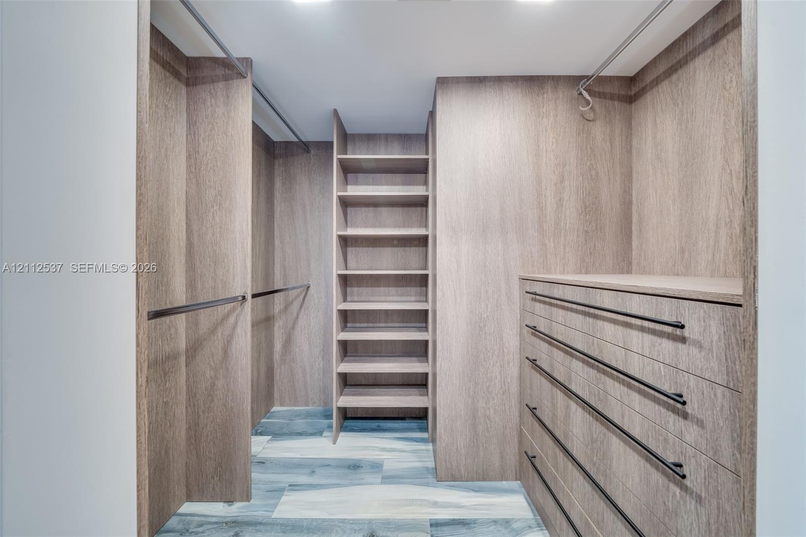 Walk-in closet featuring custom wood-finish cabinetry, floor-to-ceiling shelving, built-in dresser drawers, matte black hardware, and wood-finish flooring