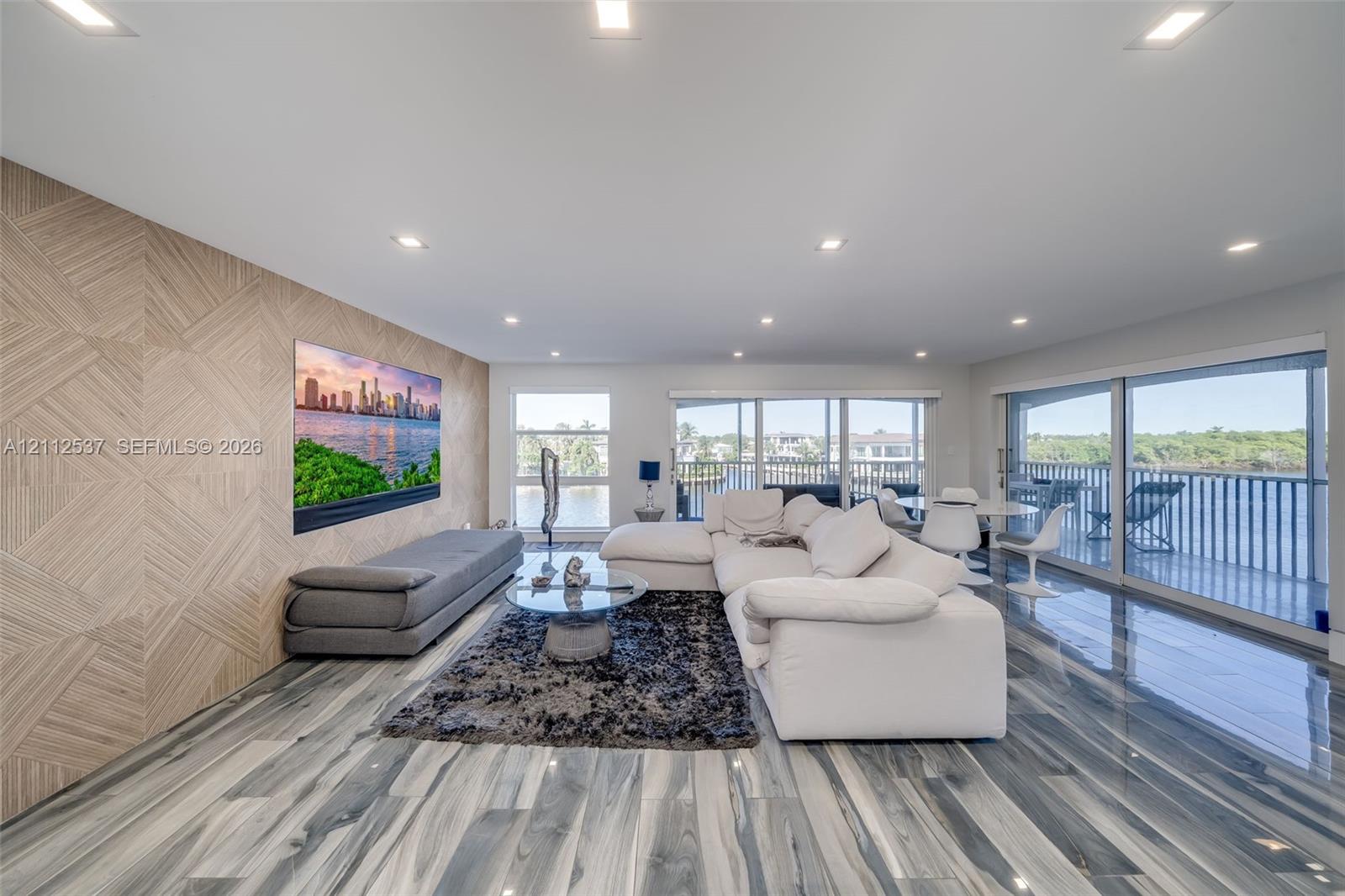 Expansive living space featuring wood-finish flooring, a textured wood-panel accent wall, recessed lighting, and floor-to-ceiling glass sliding doors