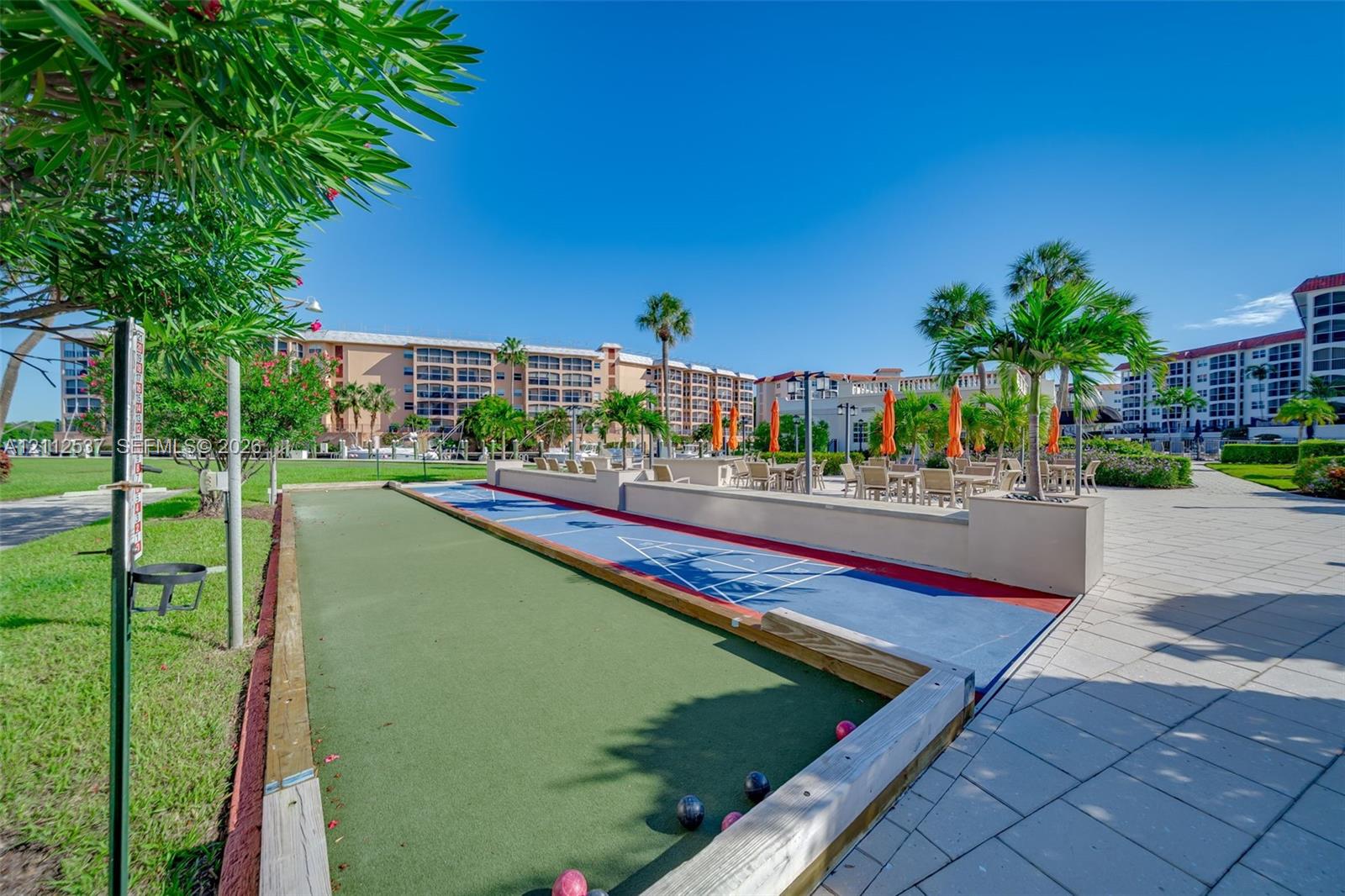 Outdoor recreation area featuring a bocce ball court, shuffleboard court, paved patio, and mature palm trees