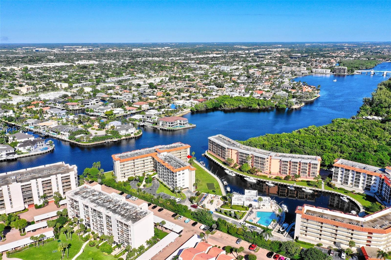 Aerial perspective of waterfront mid-rise structures featuring integrated boat slips, open-air parking, and a communal swimming pool
