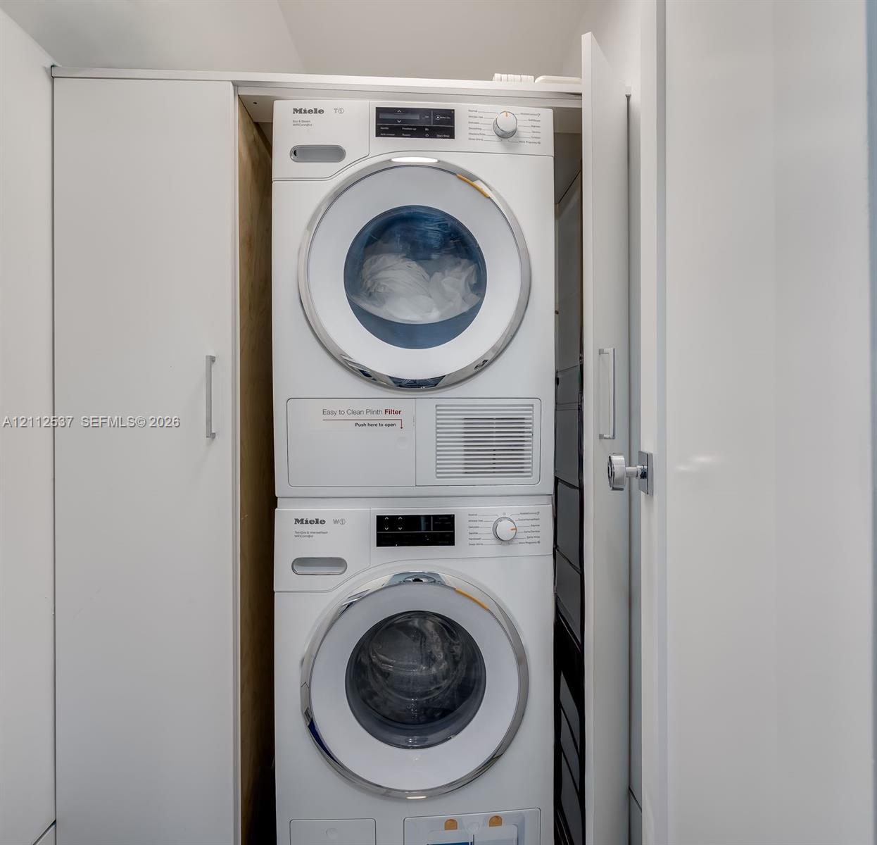 Stackable Miele washer and dryer set enclosed within custom white cabinetry featuring minimalist hardware