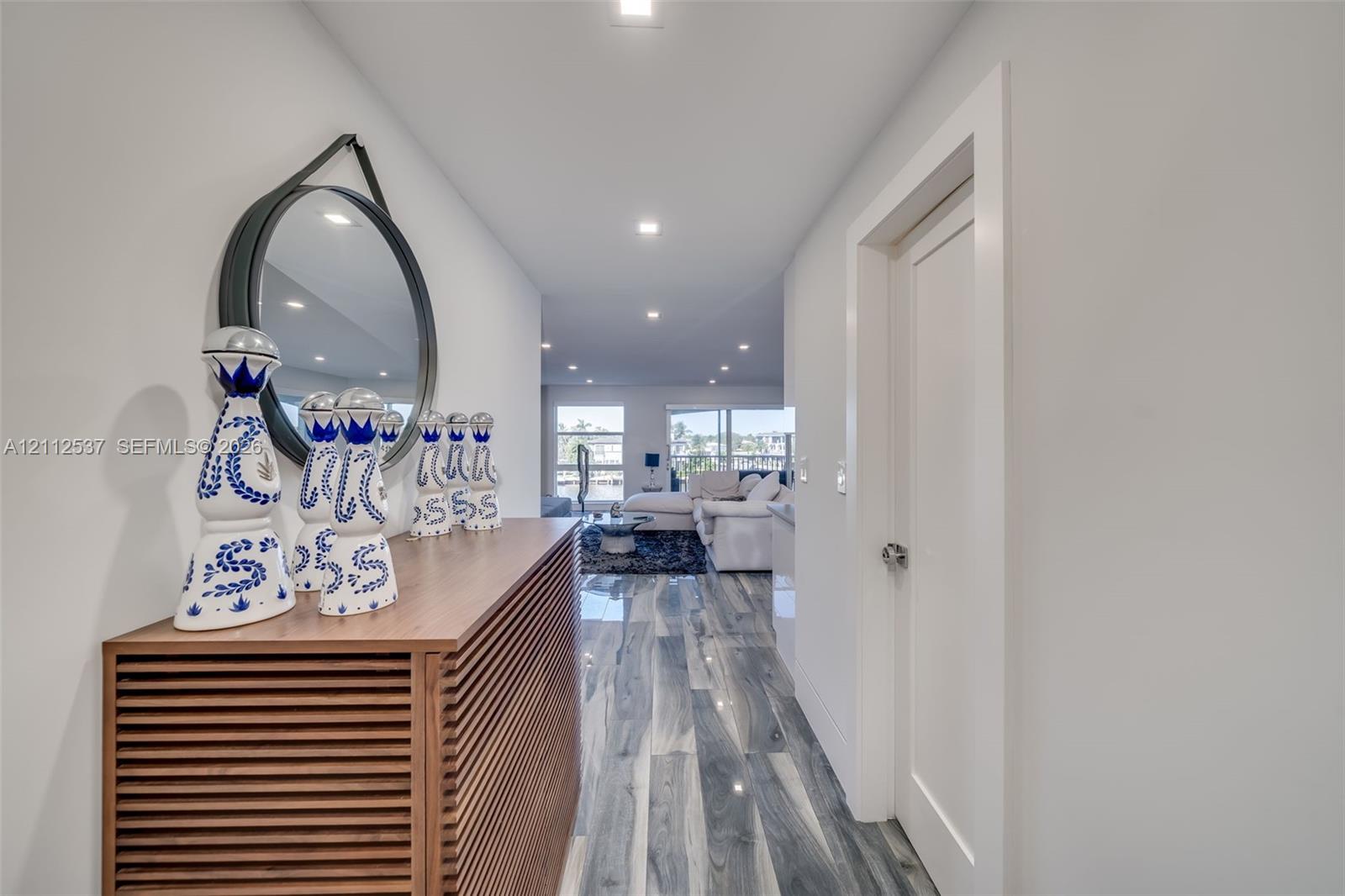 Hallway featuring high-gloss, wood-finish flooring, recessed ceiling lighting, and a minimalist door with a polished metallic handle