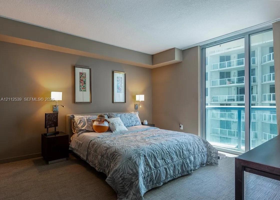 Floor-to-ceiling glass sliding doors, wall-mounted adjustable bedside lighting, and neutral-toned wall paint