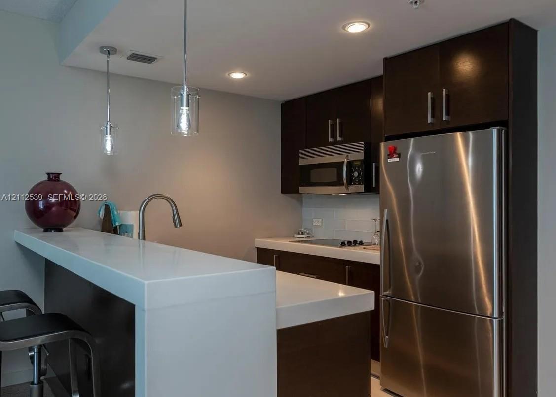 Kitchen featuring dark cabinetry, quartz countertops, stainless steel appliances, recessed lighting, and dual pendant lights Kitchen featuring dark cabinetry, quartz countertops, stainless steel appliances, recessed lighting, and dual pendant lights
