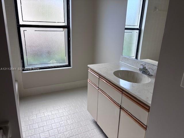 Bathroom featuring a vanity with stone-finish countertop, integrated oval basin, light-toned cabinetry, and tiled flooring Bathroom featuring a vanity with stone-finish countertop, integrated oval basin, light-toned cabinetry, and tiled flooring