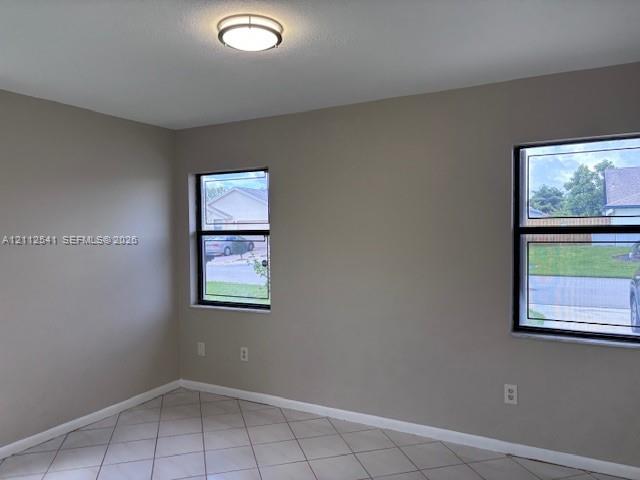 Neutral-toned interior space featuring light-colored tile flooring, flush-mount lighting, and dual windows with black frames