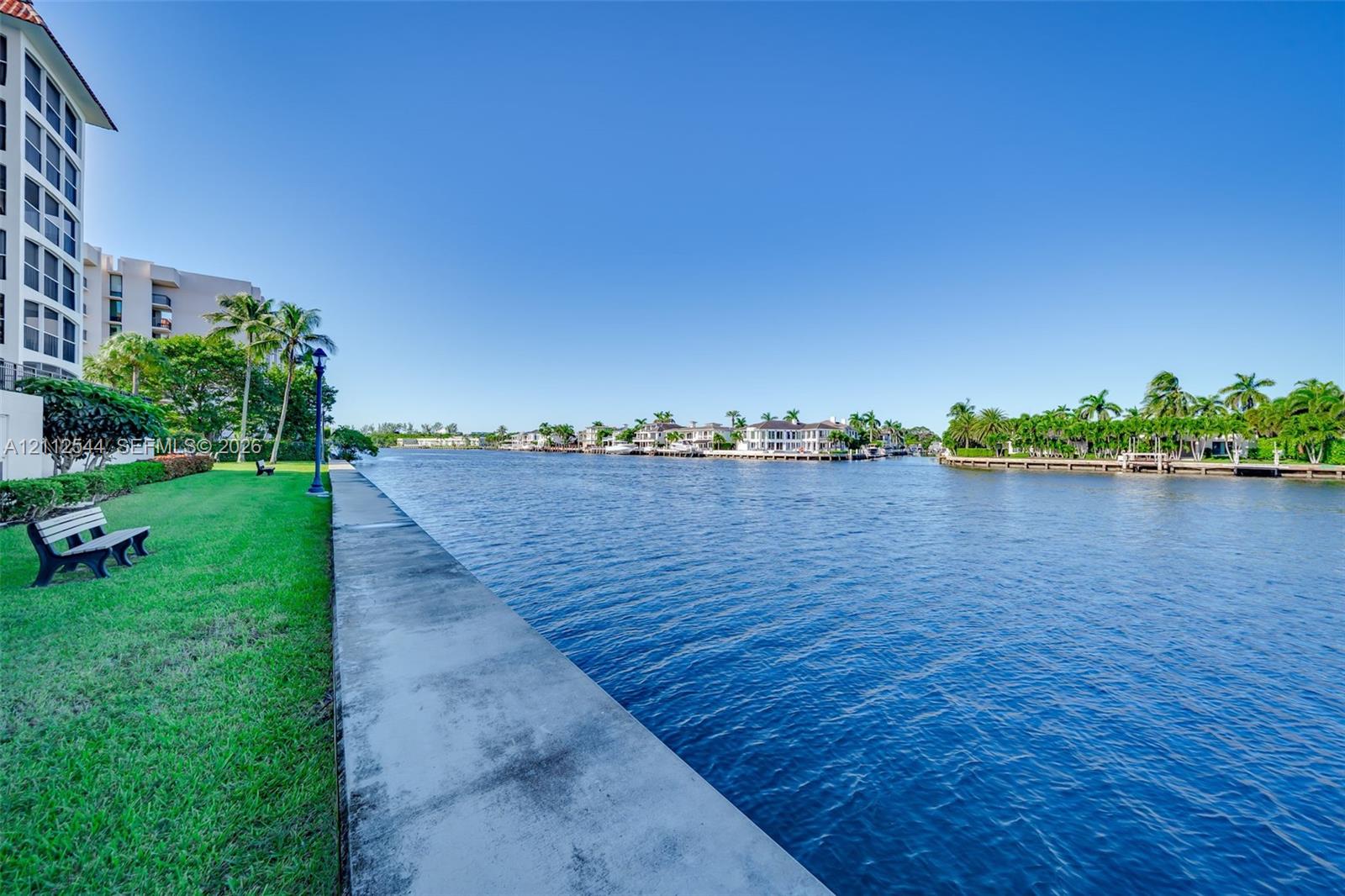 Waterfront property featuring a concrete seawall, manicured lawn, and mature palm trees