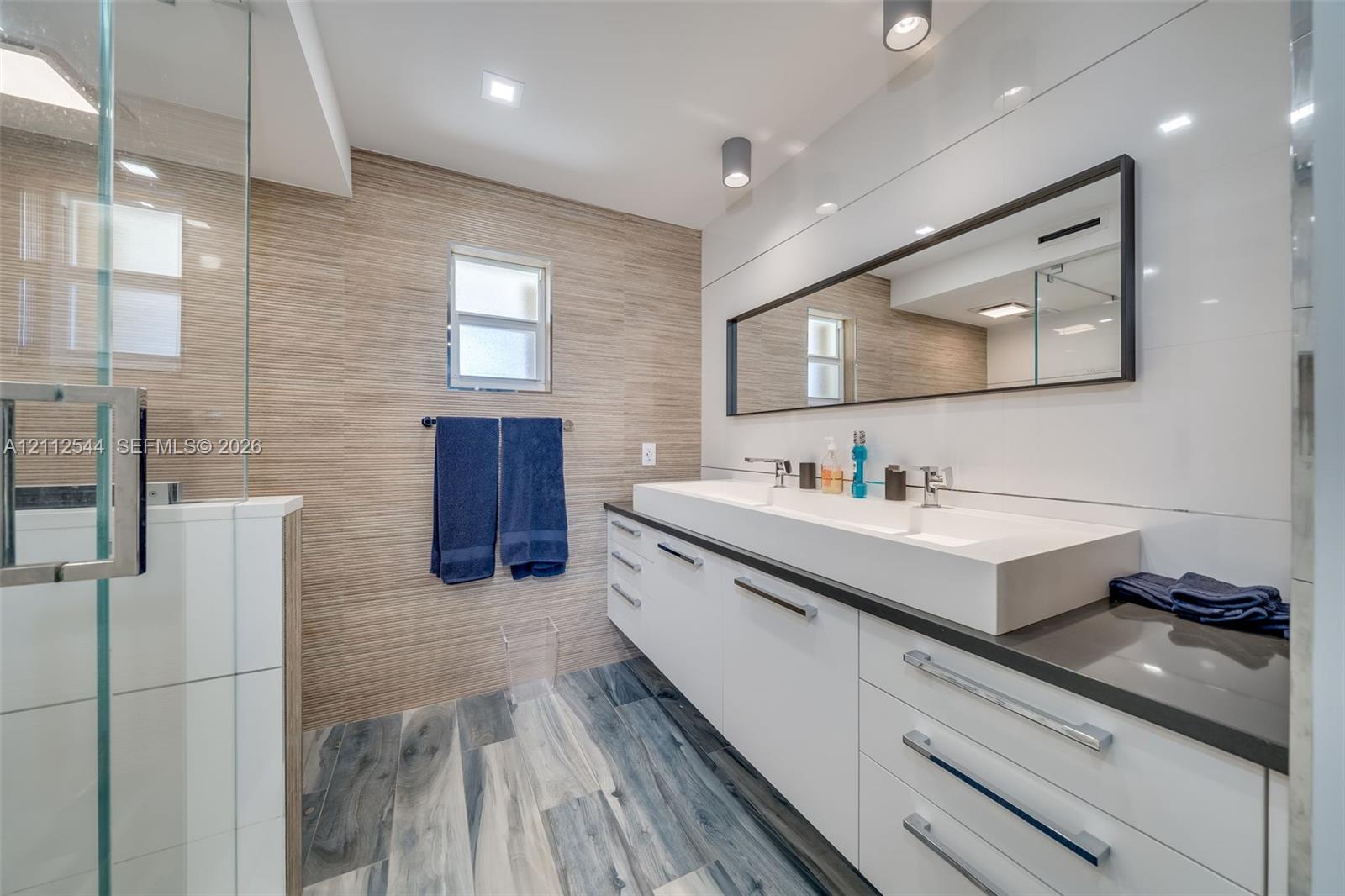 Bathroom featuring a floating double vanity with a rectangular sink, wood-finish flooring, a frameless glass shower enclosure, and full-width wall-mounted mirror