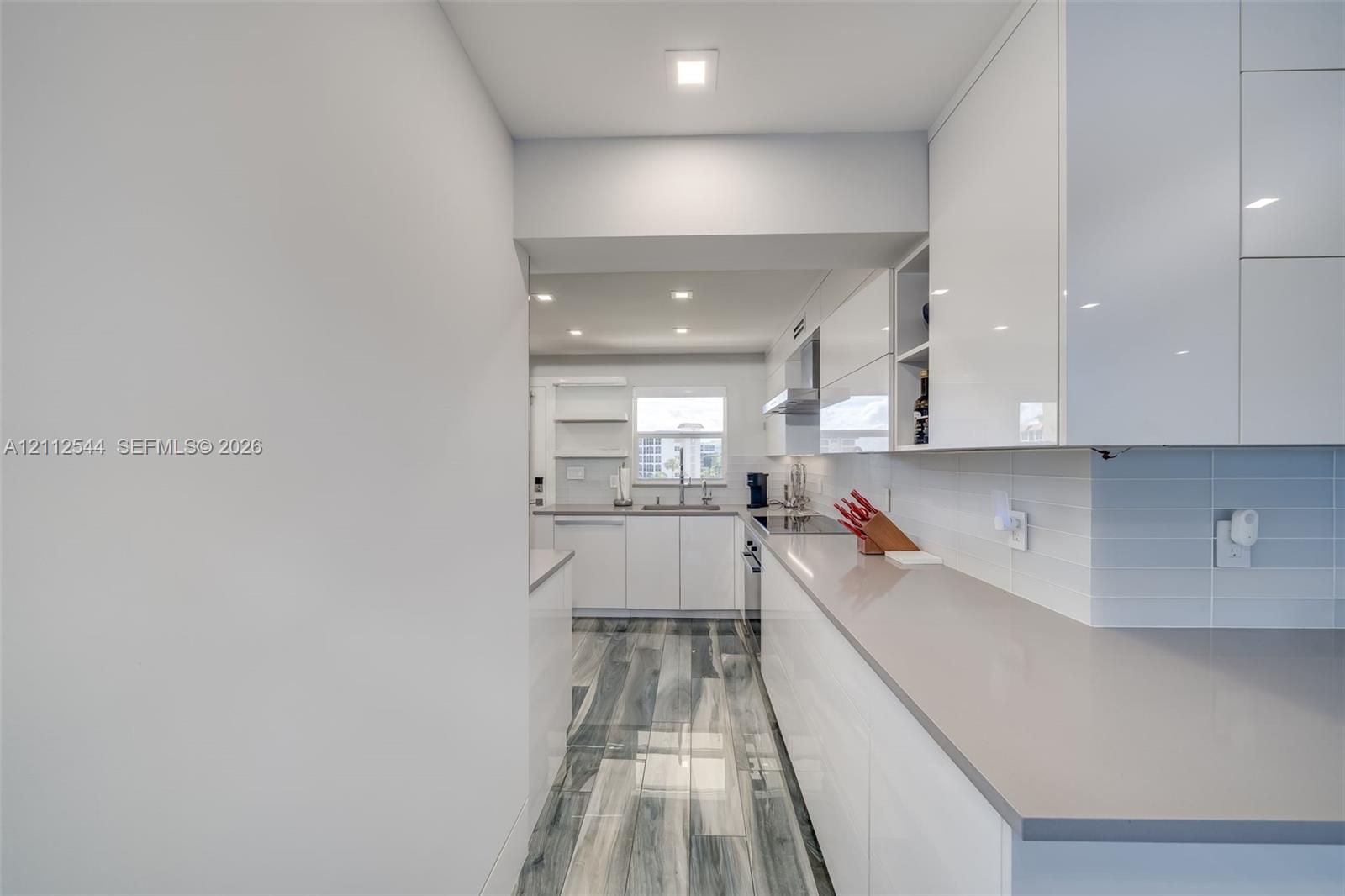 Kitchen featuring high-gloss cabinetry, solid-surface countertops, tile backsplash, wood-finish flooring, and recessed ceiling lighting