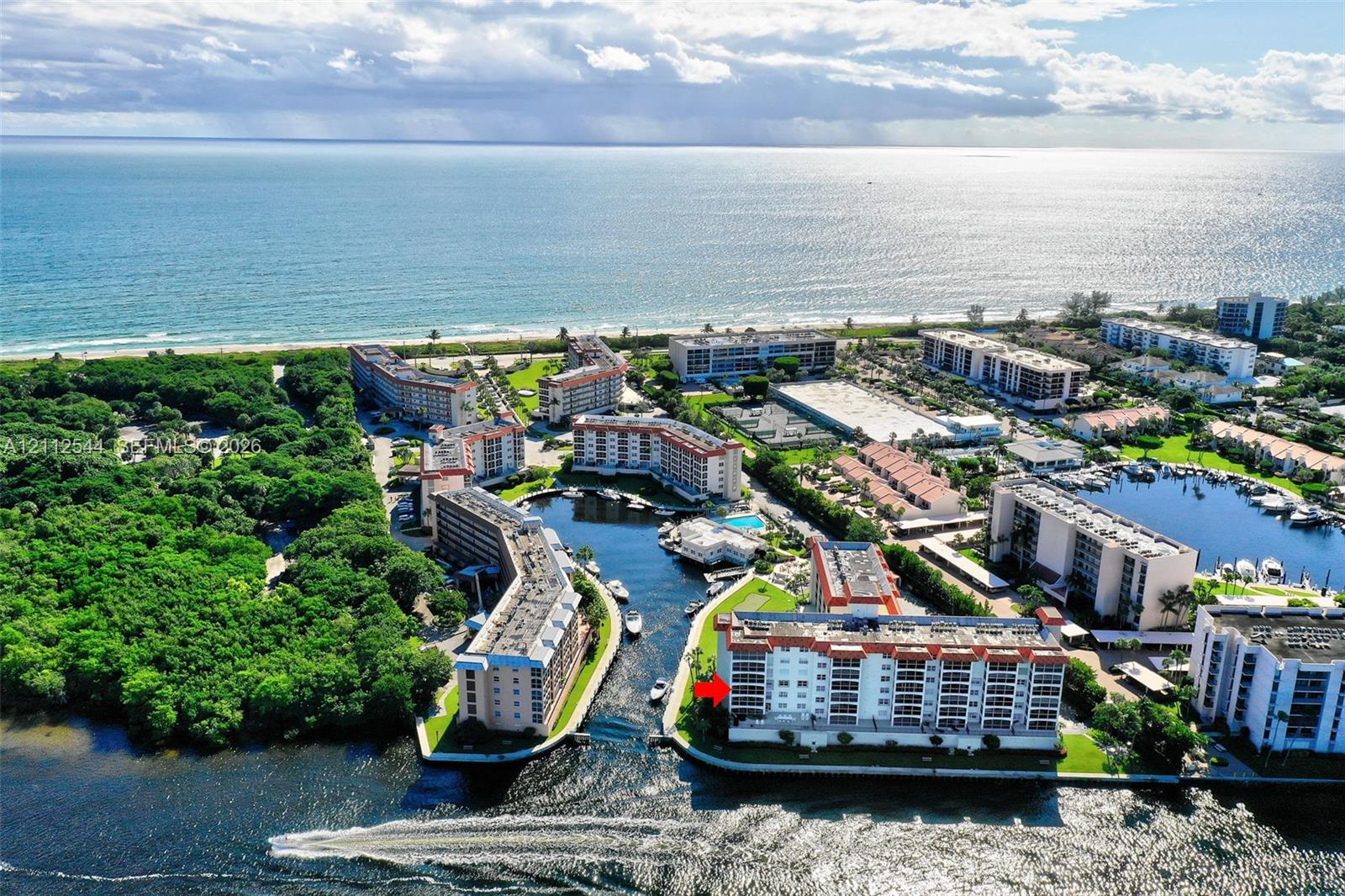Aerial perspective featuring a waterfront multi-story building positioned along a canal with direct ocean access, surrounded by dense coastal vegetation and maintained grounds