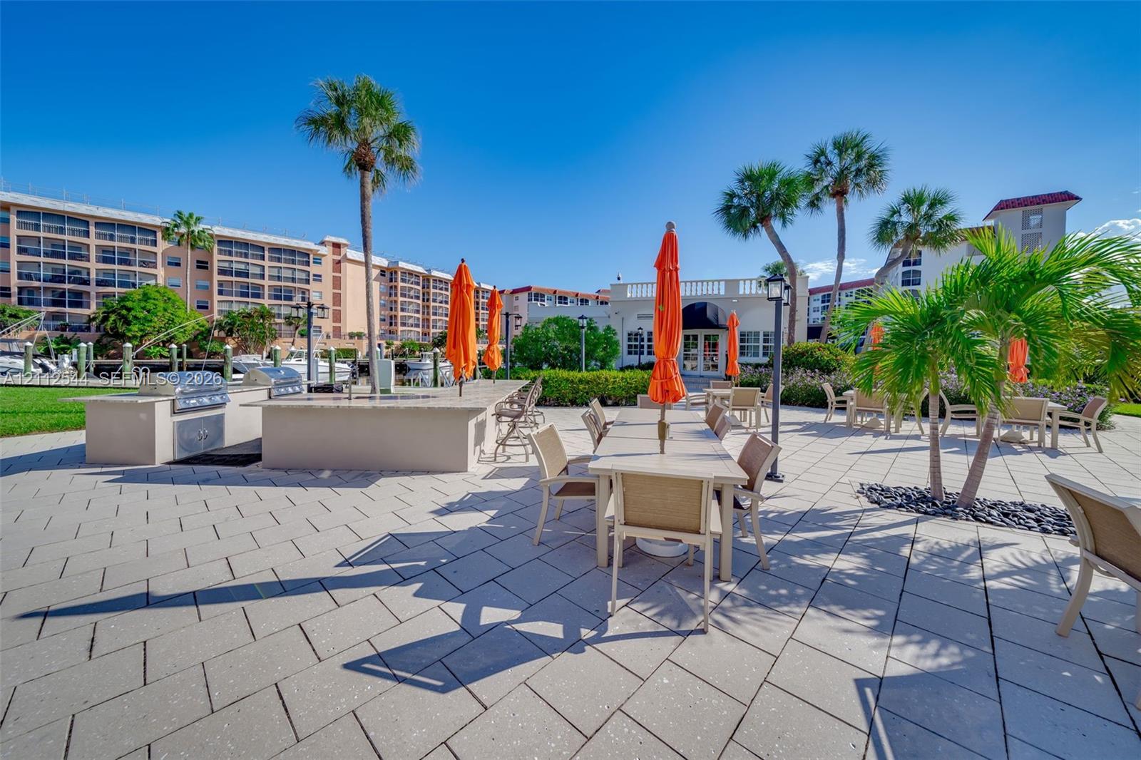 Outdoor patio area featuring stone-paver flooring, a built-in outdoor kitchen with stainless steel appliances, and mature palm trees
