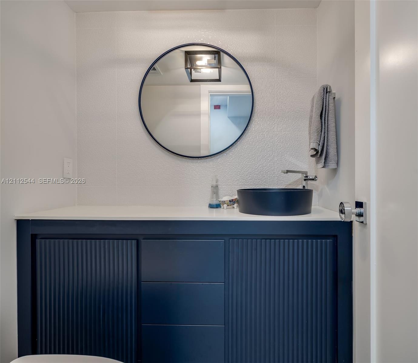 Navy blue fluted vanity with a white countertop, round black-framed mirror, and matte black vessel sink