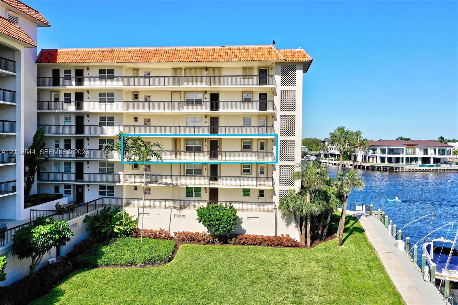 Multi-story waterfront residential building featuring a terracotta tile roof, wrap-around balconies with metal railings, and direct access to a private dock