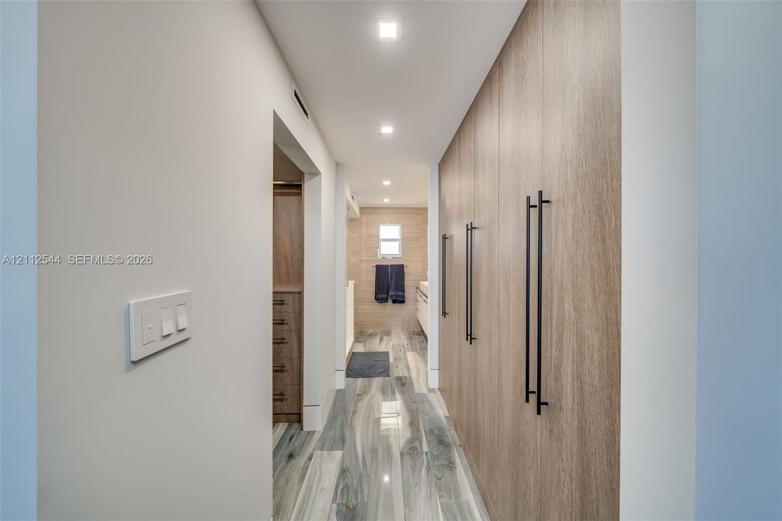 Floor-to-ceiling built-in wood-finish cabinetry featuring matte black hardware, recessed ceiling lighting, and porcelain tile flooring with a marble-pattern finish