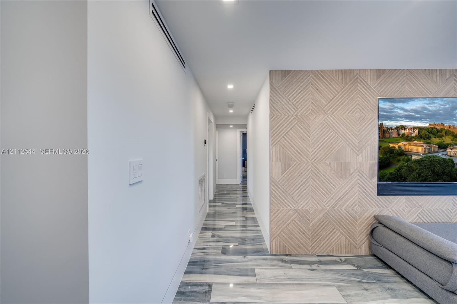 Hallway featuring large-format polished tile flooring, geometric wood-patterned accent wall, and recessed ceiling lighting