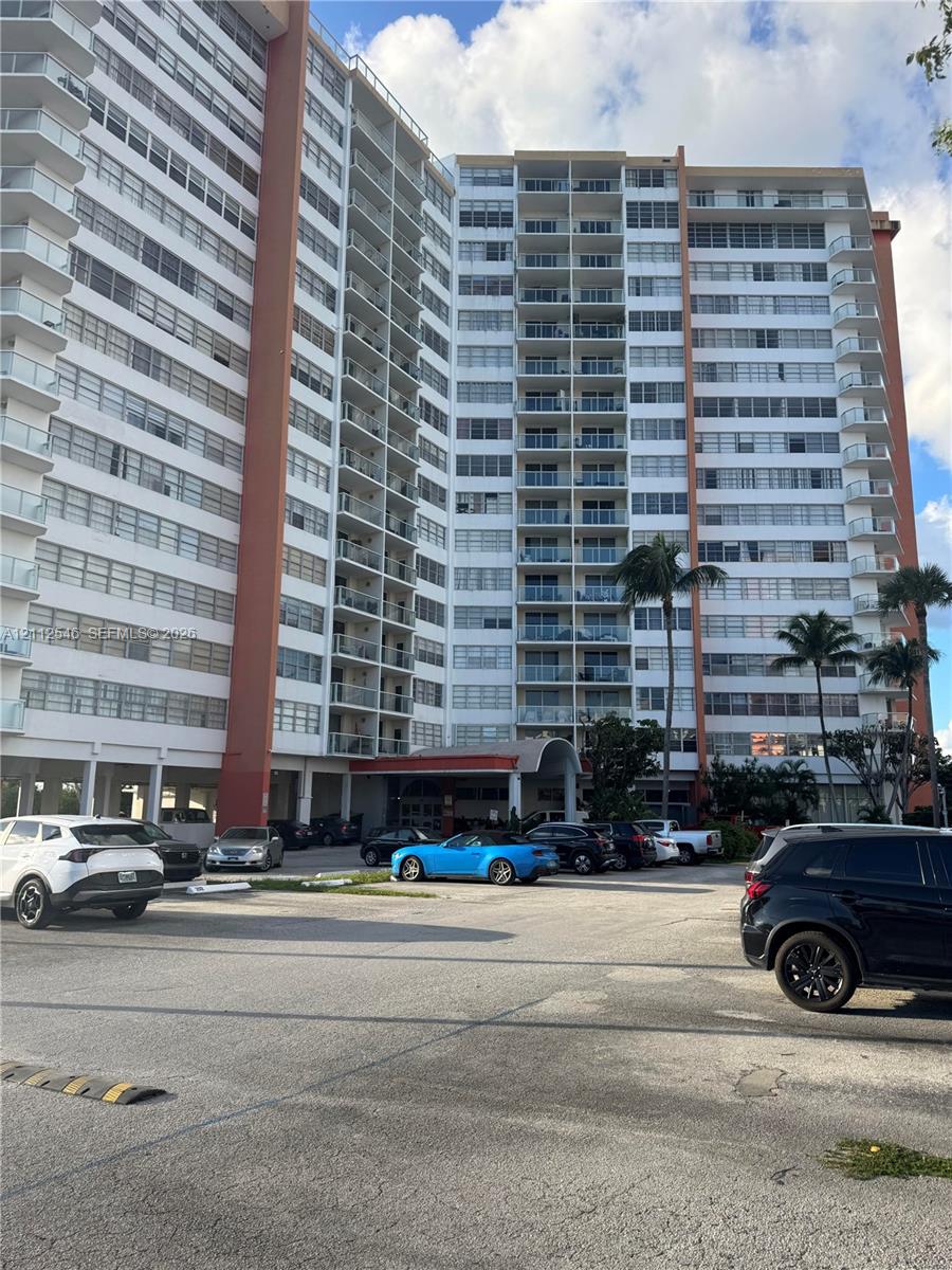 High-rise residential building featuring stacked private balconies, a covered porte-cochre entry, and landscaped grounds with mature palm trees