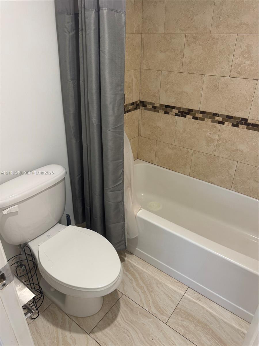 Bathtub with a shower surround featuring large-format stone-finish wall tiles and a decorative mosaic inlay, paired with stone-finish floor tiling