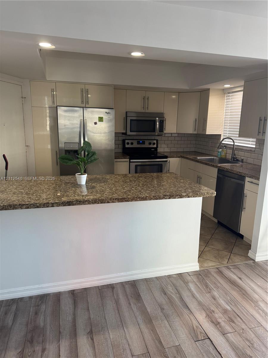 Kitchen featuring a breakfast bar, stone-surface countertops, subway tile backsplash, stainless steel appliances, and wood-finish flooring