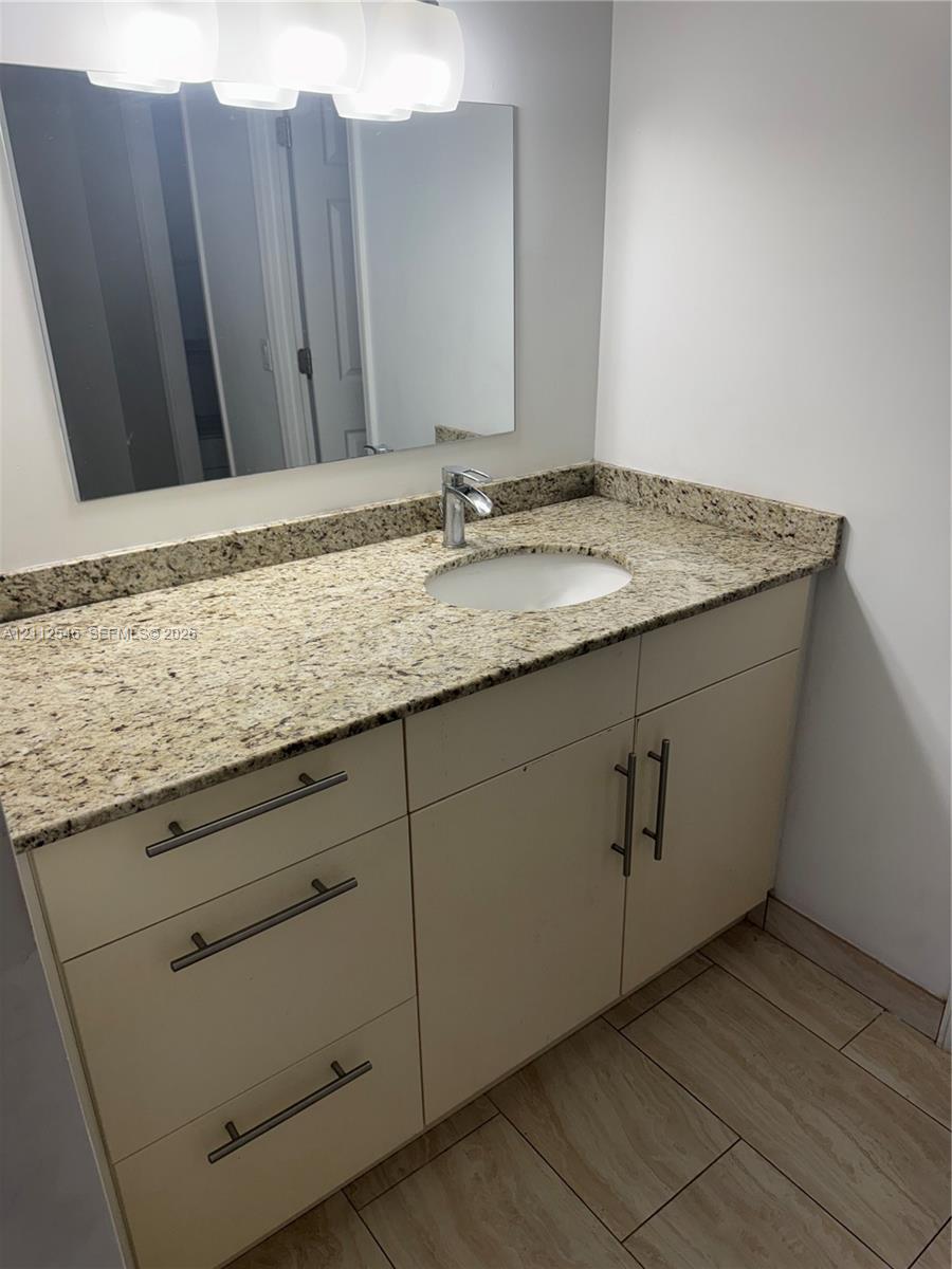 Vanity featuring stone-finish countertop, undermount sink, brushed metal hardware, and wood-finish tile flooring