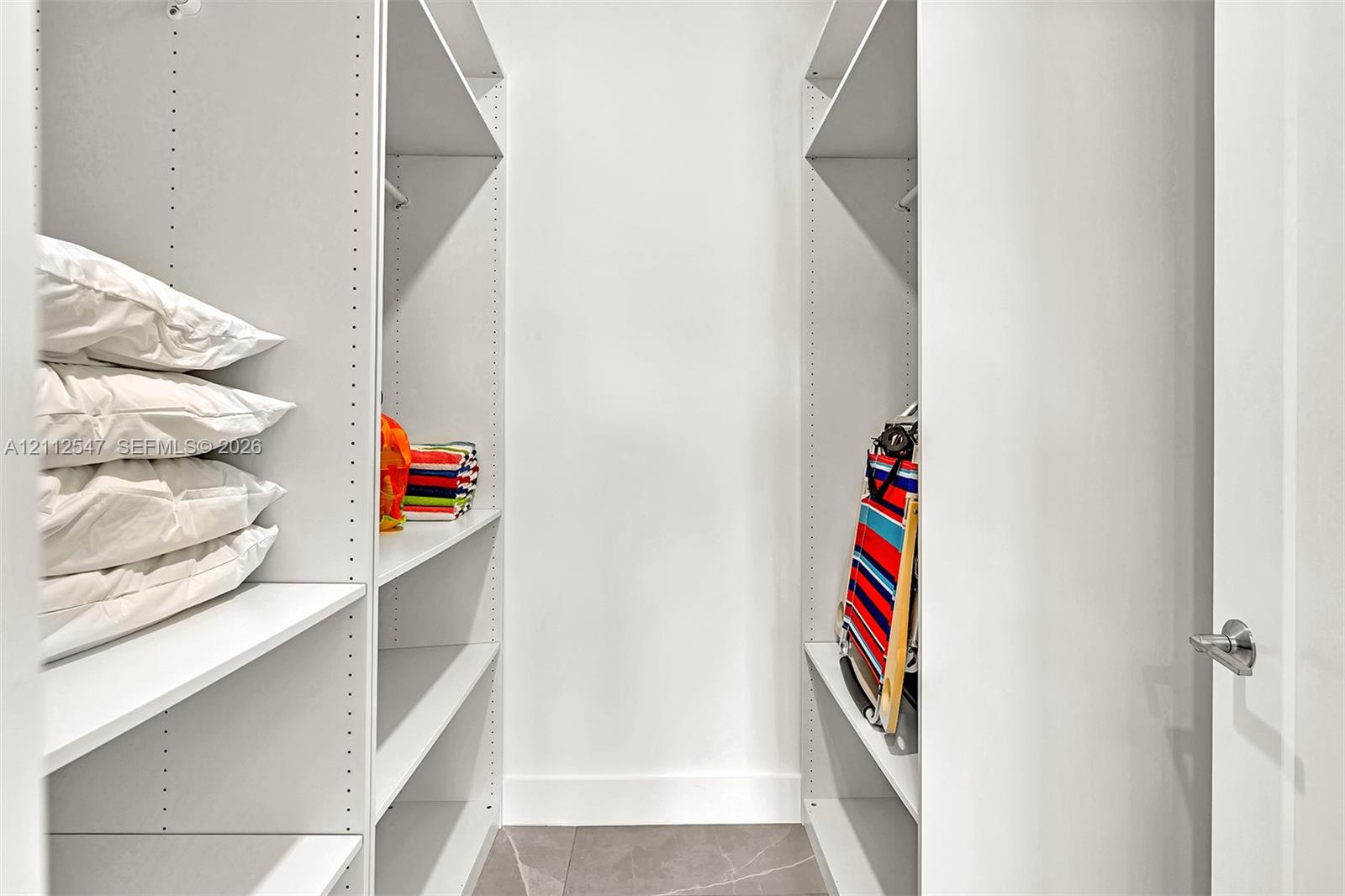 Custom reach-in storage system with white finish, adjustable shelving, integrated garment rods, and large-format tile flooring