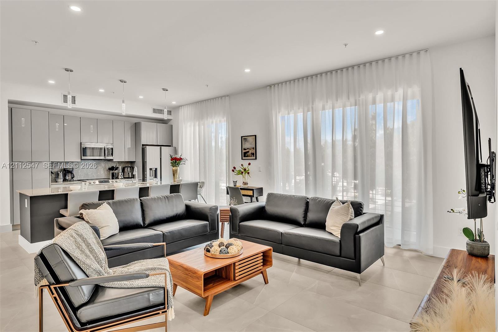Open-concept interior featuring high-gloss cabinetry, stone-surface kitchen countertops, large-format tile flooring, and floor-to-ceiling windows with integrated recessed lighting