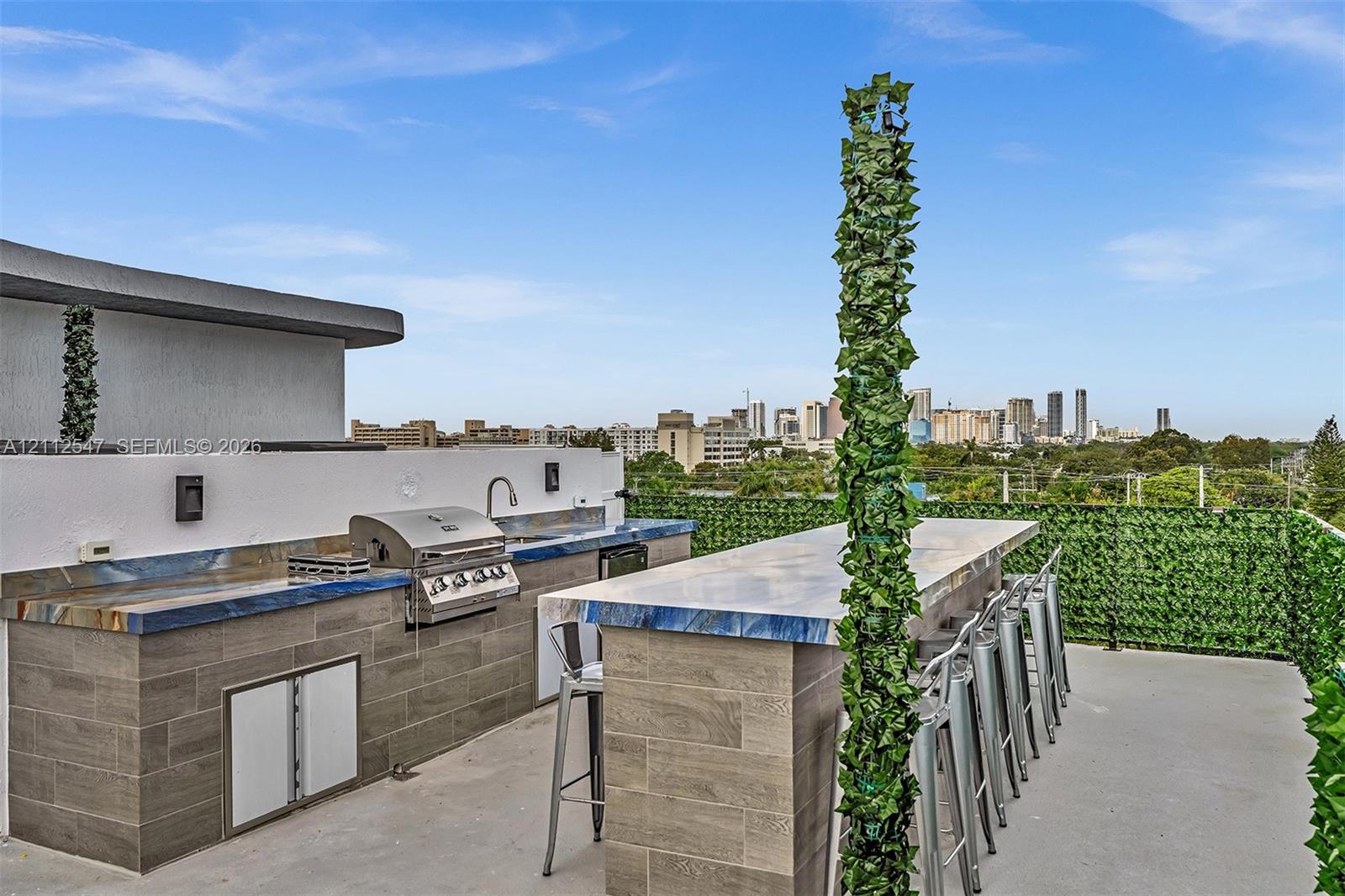 Rooftop terrace featuring a built-in outdoor kitchen with stainless steel grill, stone-finish countertops, tile-clad cabinetry, and an integrated bar counter
