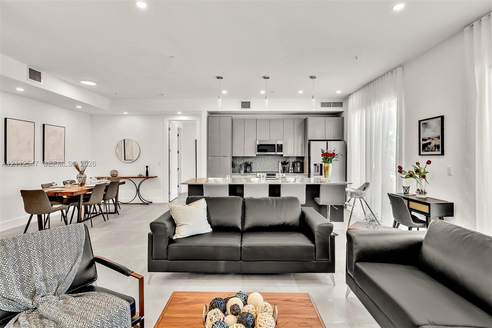 Open-concept living space featuring high-gloss cabinetry, a central kitchen island, recessed lighting, and large-format tile flooring