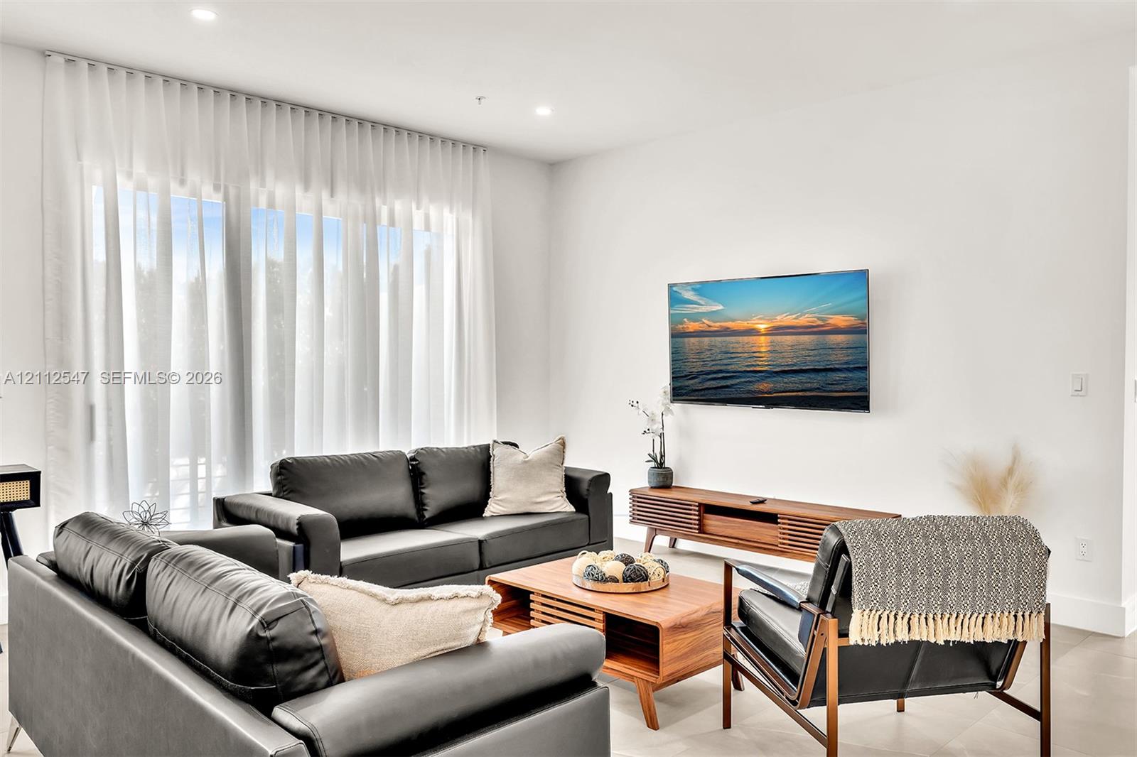 Full-height windows with floor-to-ceiling sheer drapery, recessed lighting, and neutral wall finishes