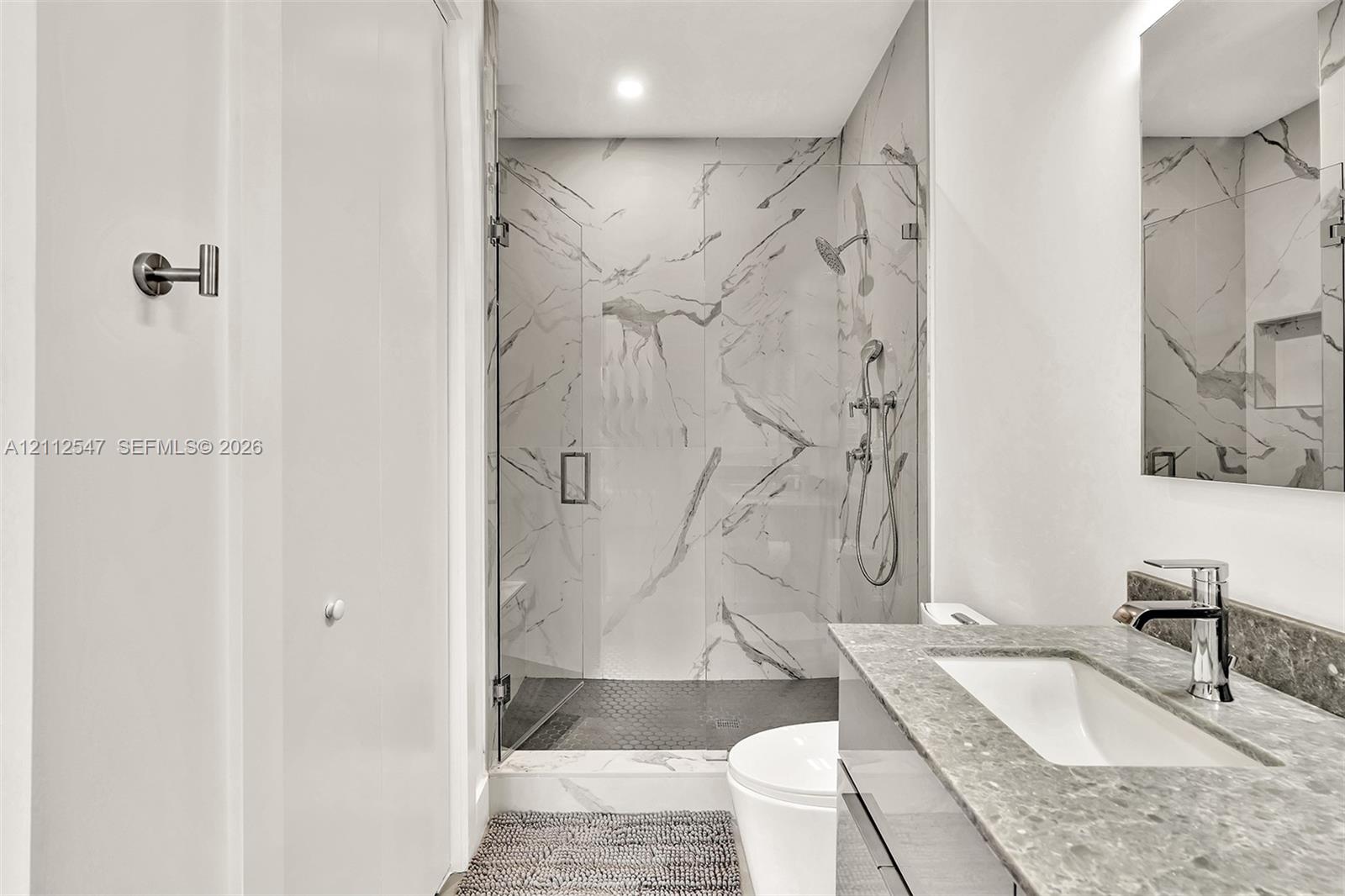 Bathroom featuring a walk-in shower with large-format stone-patterned tile, frameless glass enclosure, wall-mounted shower hardware, floating vanity with a stone countertop, and an integrated rectangular sink