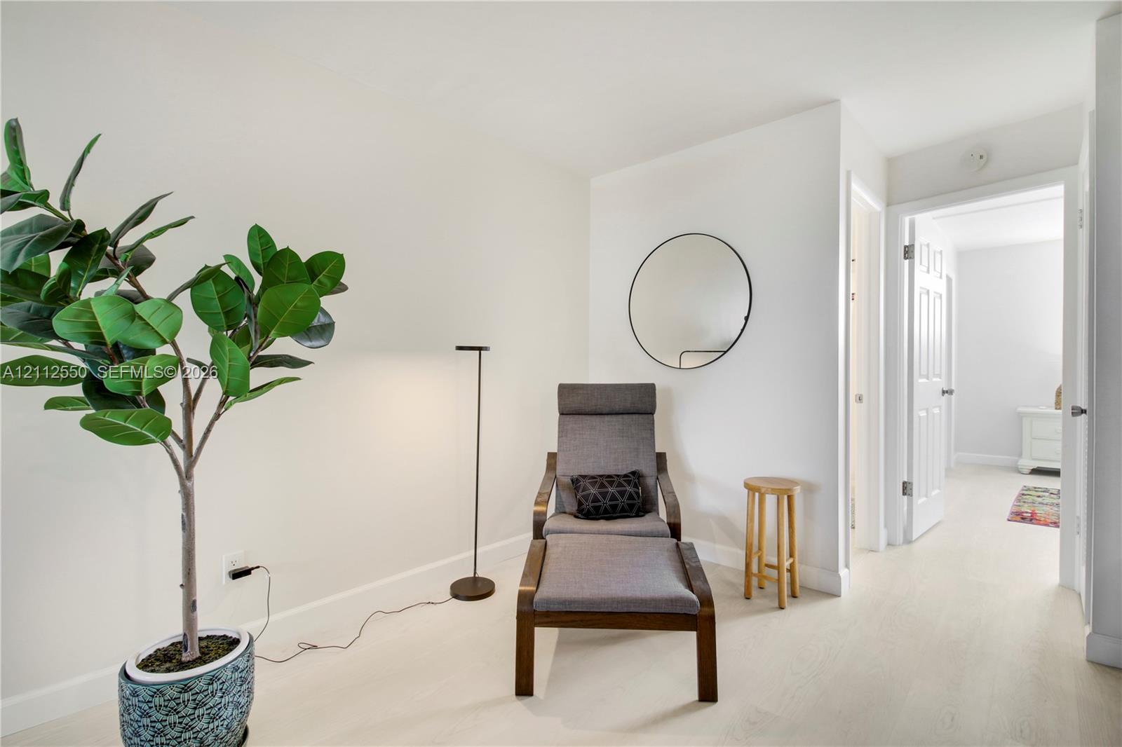 Neutral interior featuring wood-finish flooring, a wall-mounted circular mirror, and multi-panel interior doors