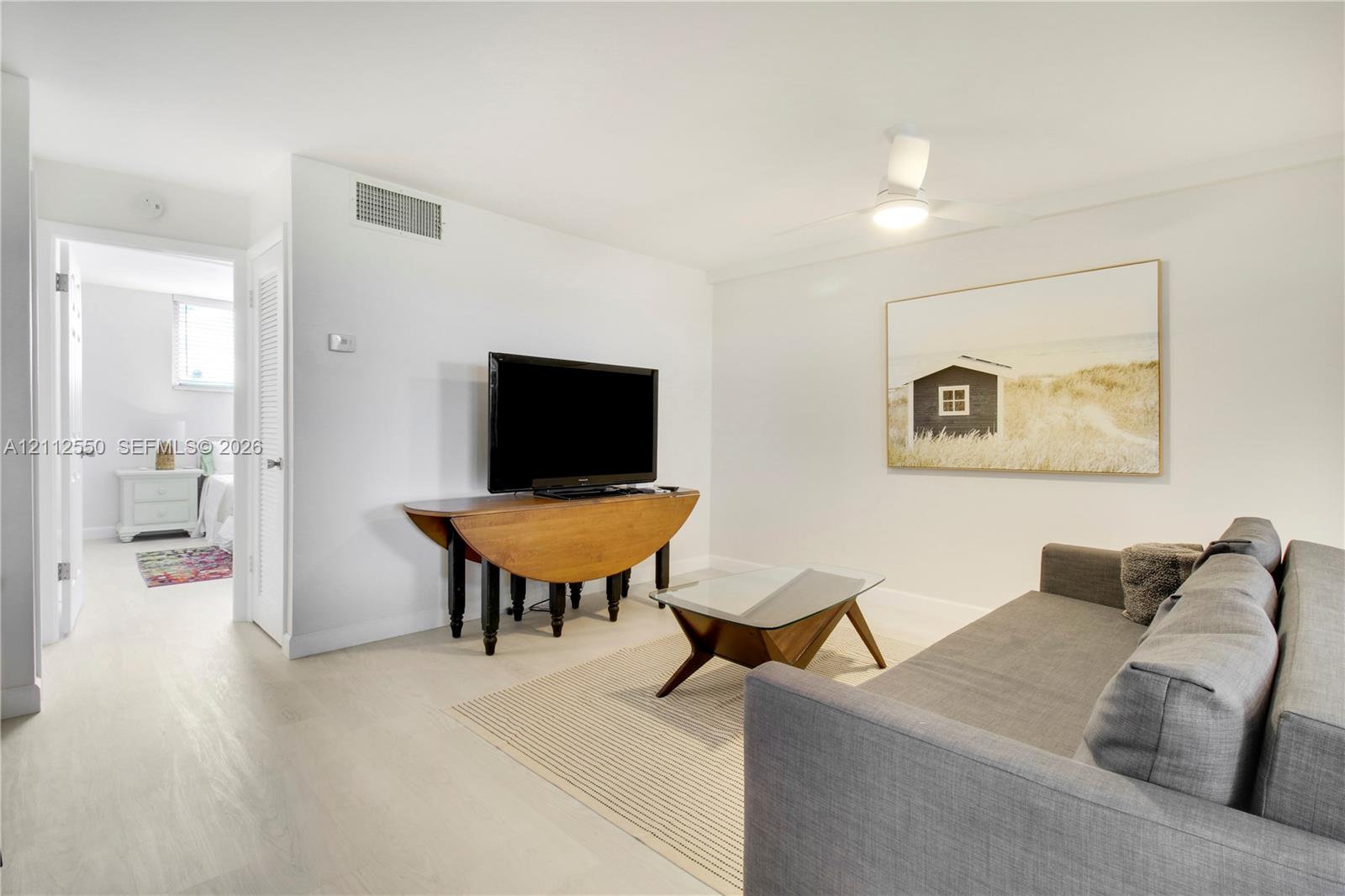 Neutral-toned interior featuring continuous light-colored flooring, white walls, and a ceiling-mounted light fixture with an integrated fan