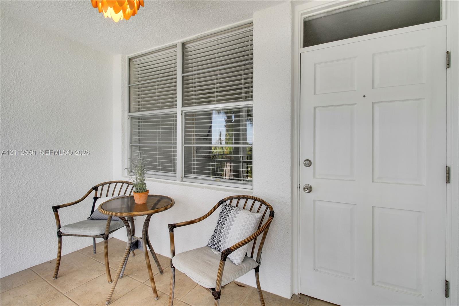 Covered entry featuring a white panel door with transom window, ceramic tile flooring, and integrated blinds