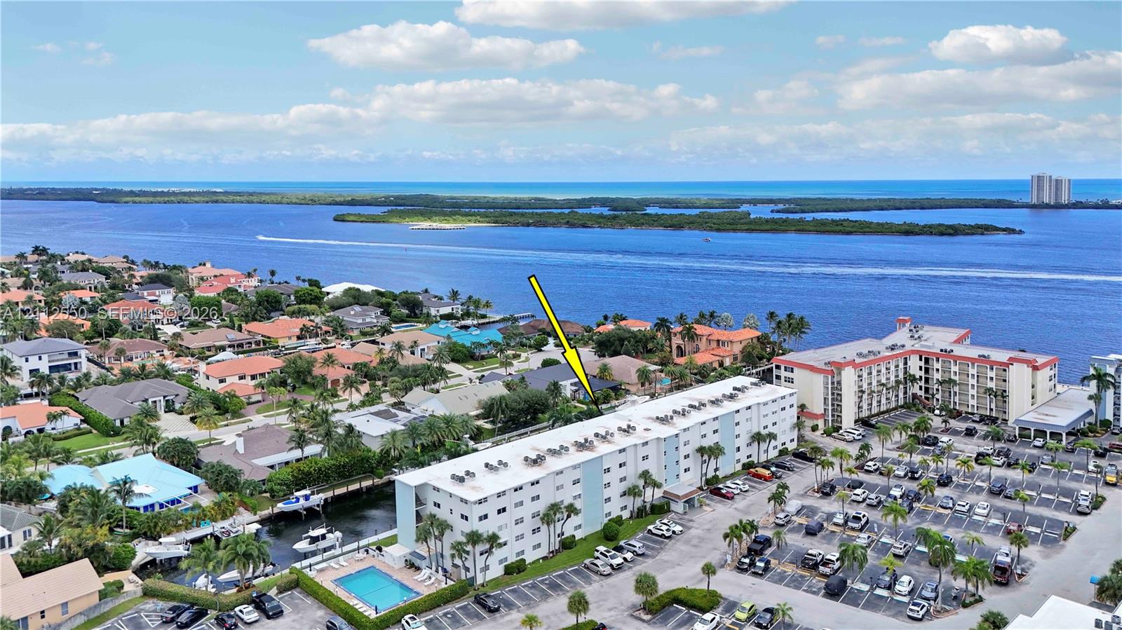 Aerial perspective of a multi-story residential building featuring a private swimming pool, dedicated parking area, and canal-front positioning