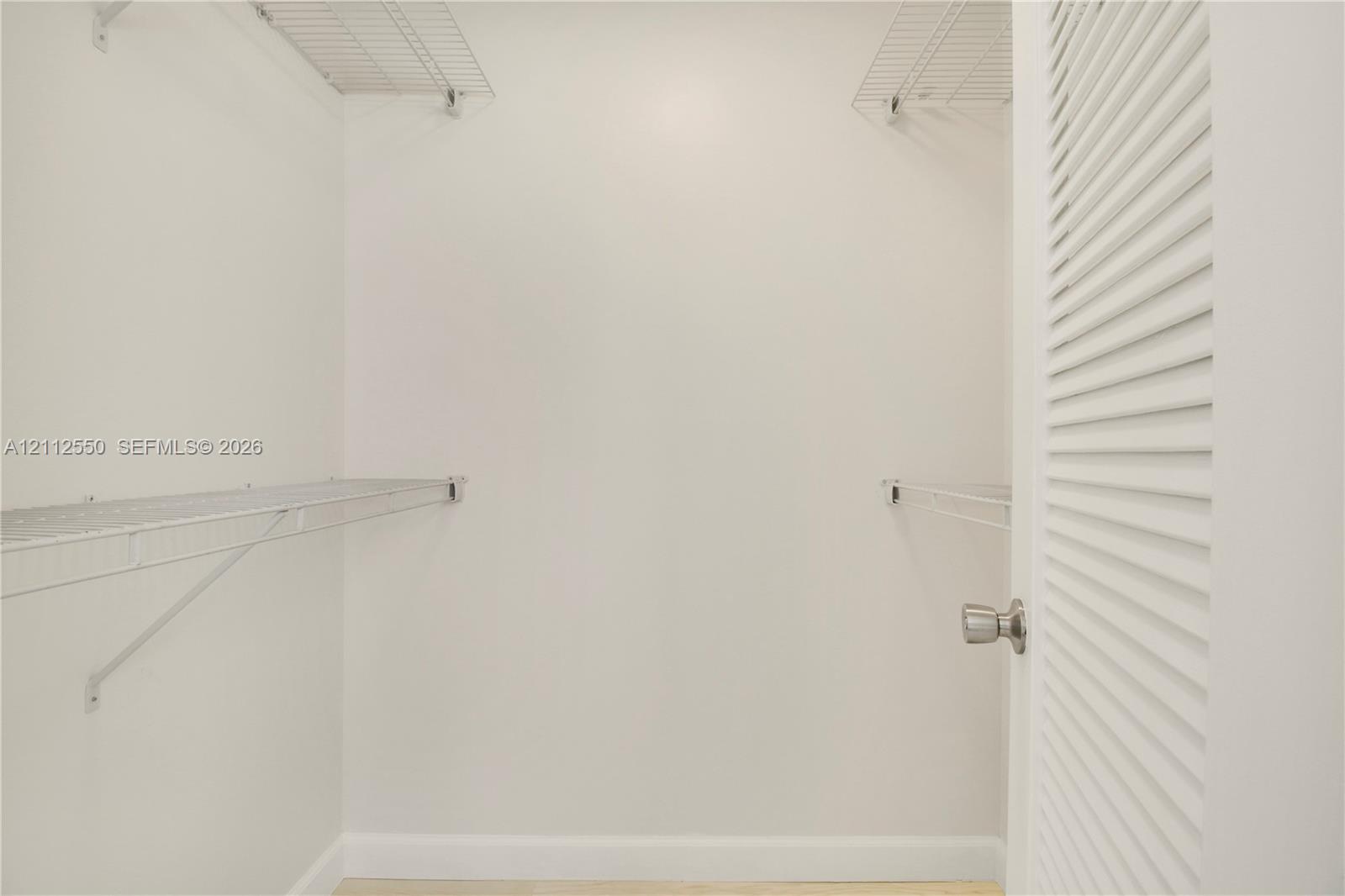 Storage area featuring tiered wire shelving and a louvered door with a metallic knob