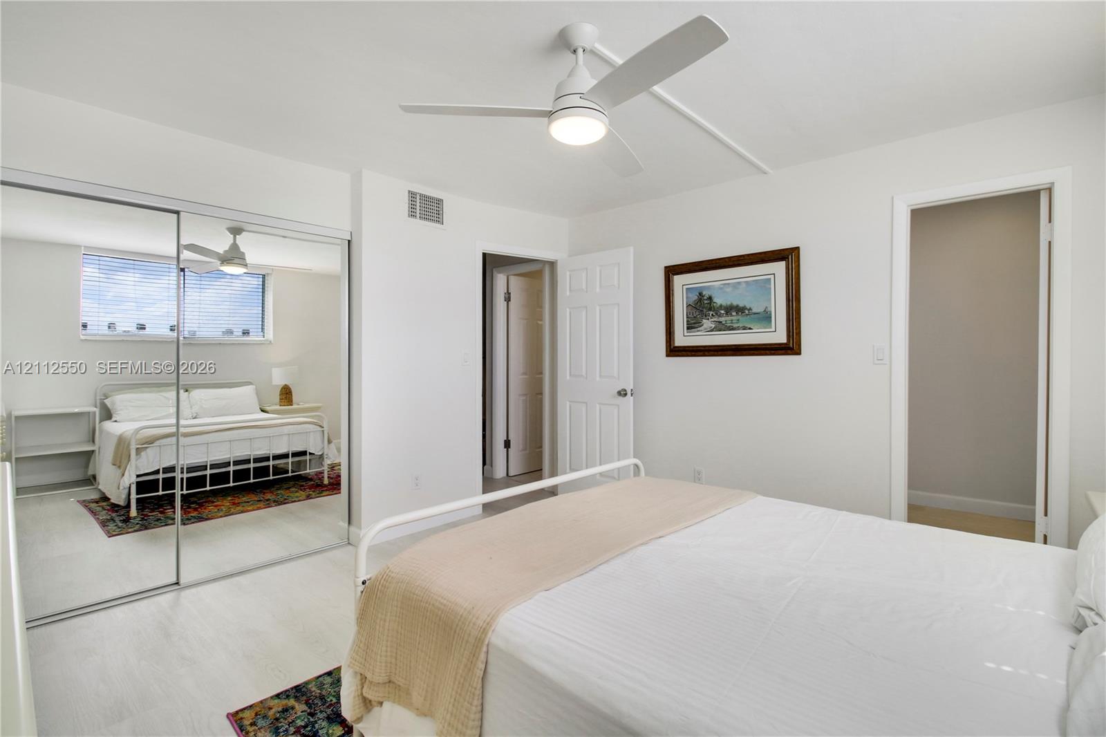 Light-toned wood-finish flooring, ceiling fan with integrated lighting, and mirrored sliding closet doors