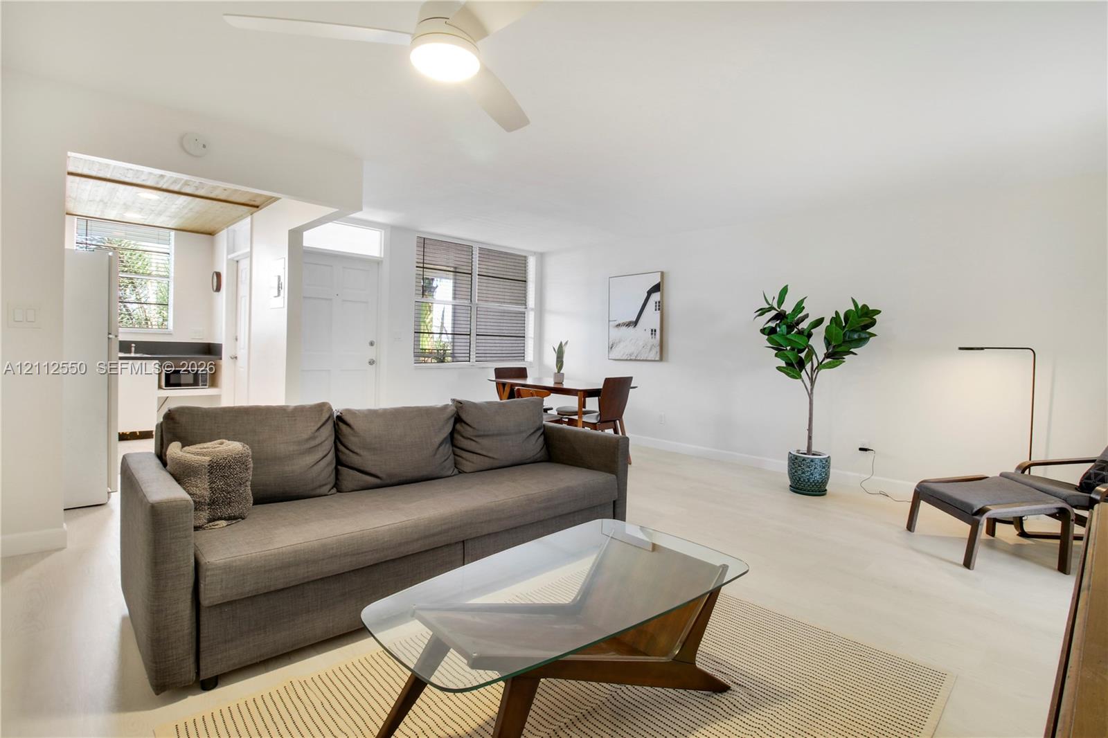 Open interior featuring white-tone flooring, neutral wall finishes, multi-pane windows with integrated blinds, and a central ceiling fan with integrated lighting