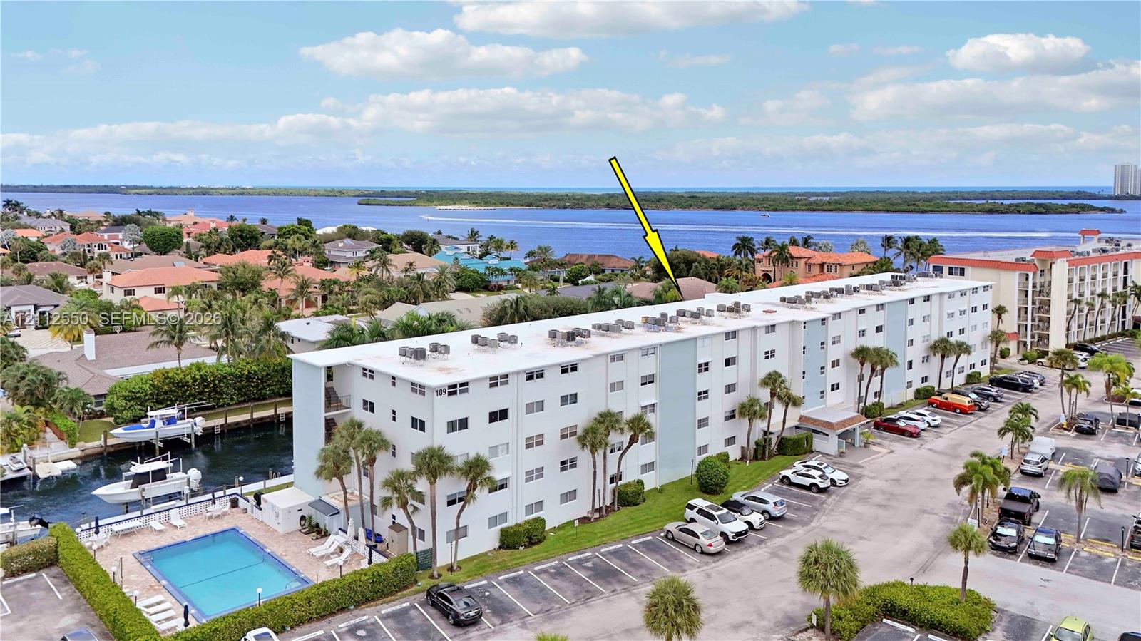 Multi-story residential building featuring an outdoor swimming pool, paved surface parking, and canal frontage with boat slips