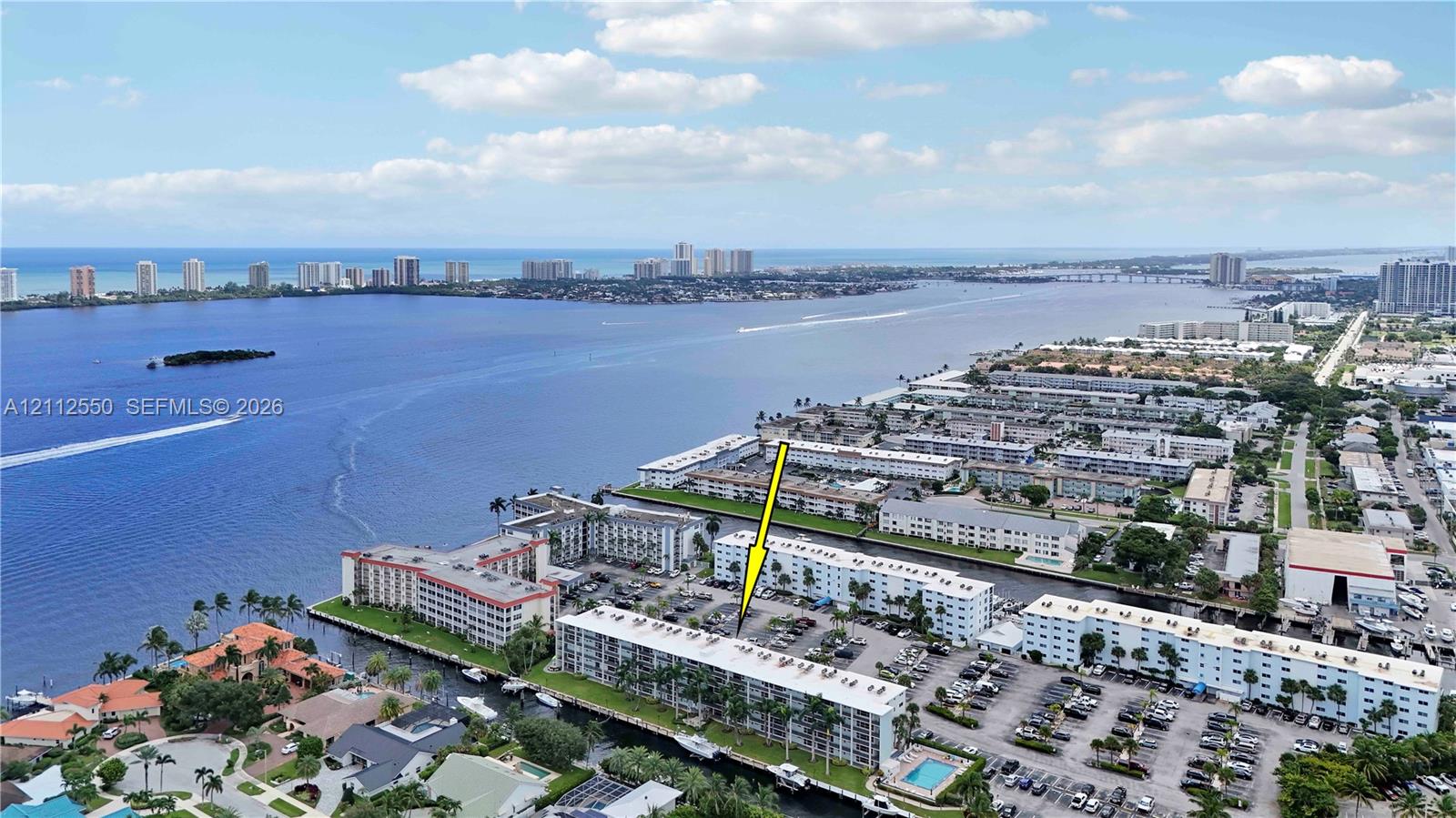 Aerial perspective featuring a multi-story residential building located along a waterfront canal with proximity to the coastline