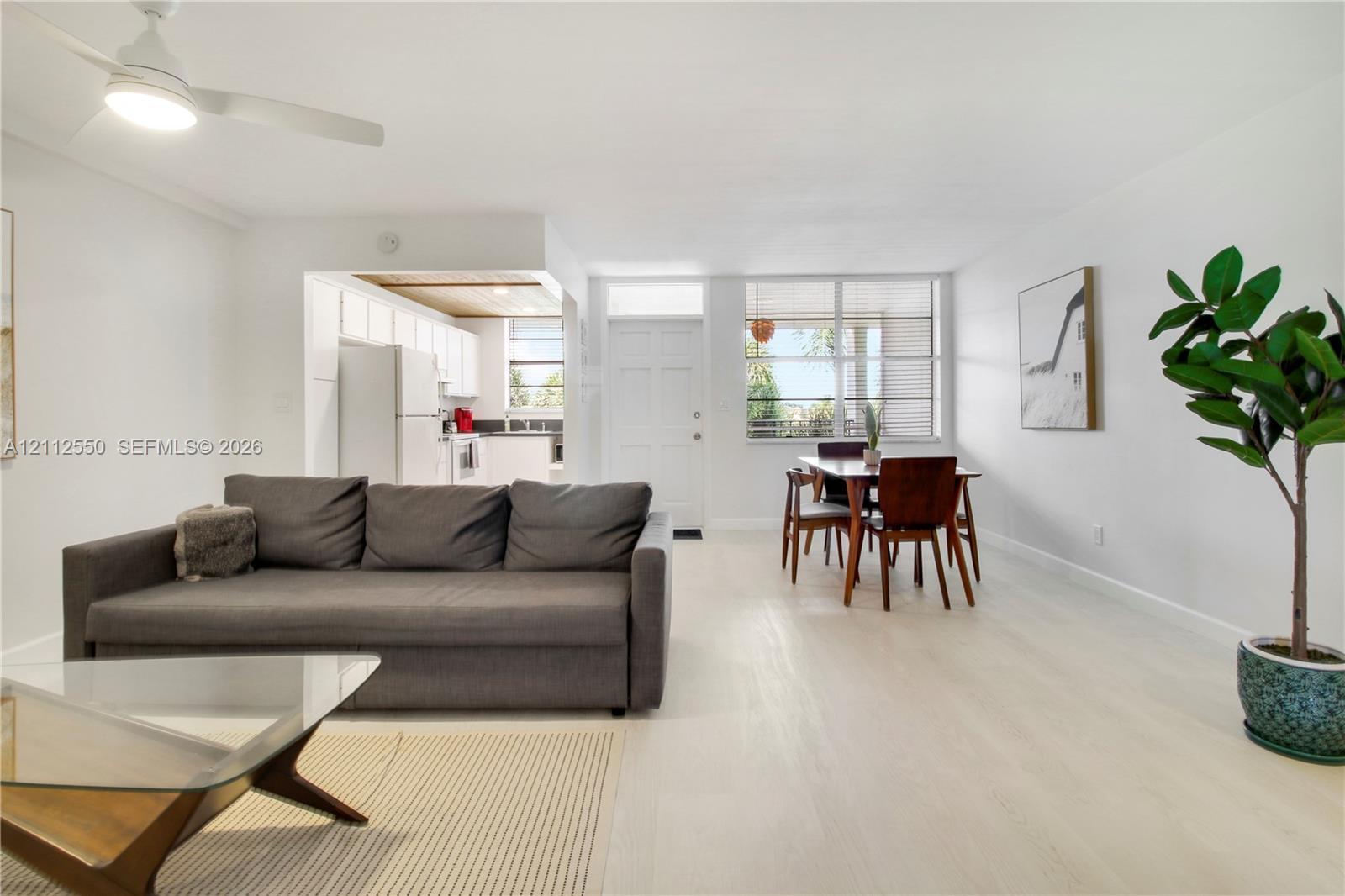 Open-concept living space featuring wood-finish flooring, white cabinetry, a ceiling-mounted light fixture, and multi-pane windows