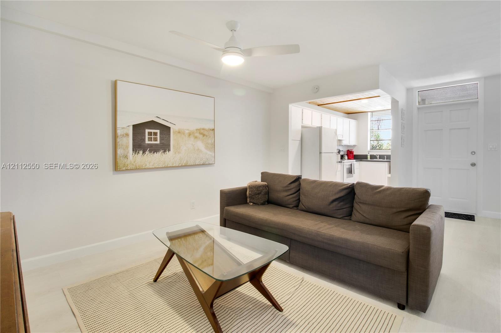 Neutral-toned interior featuring light wood-finish flooring, a ceiling-mounted light fixture with fan, and a paneled entry door with an upper transom window