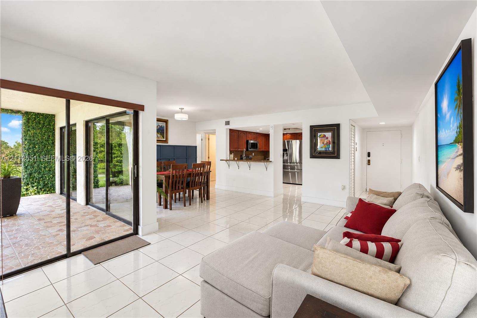 Open-concept living space featuring high-gloss tile flooring, sliding glass door access to a covered patio, and a kitchen pass-through counter