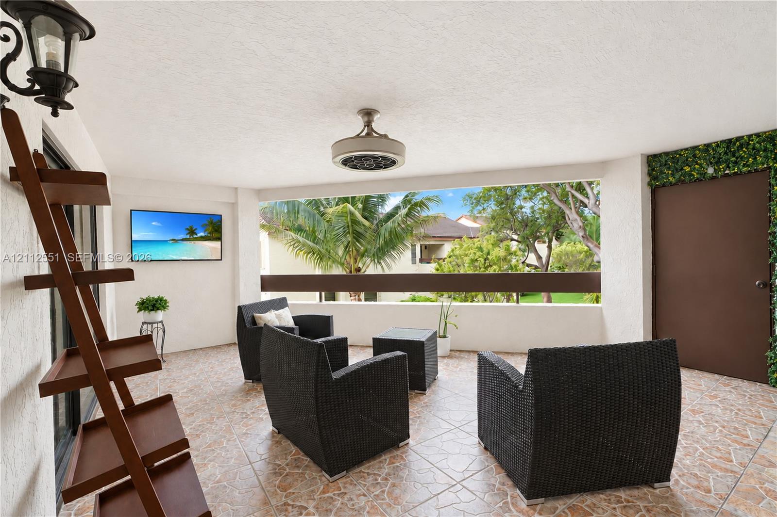 Covered outdoor living space featuring tiled flooring, a ceiling fan, a wall-mounted television, and a half-wall railing