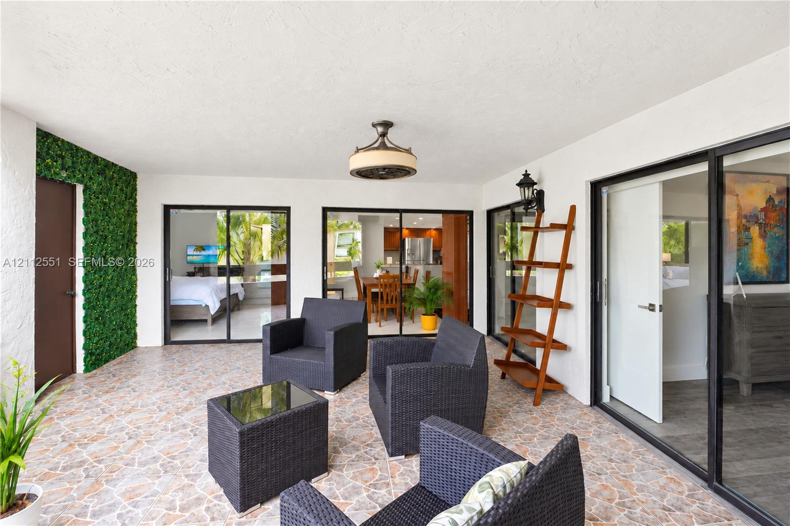 Covered patio featuring stone-tile flooring, decorative green wall accent, ceiling-mounted light fixture, and multiple sliding glass door entries